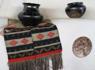 Hopi sash, ca. 1880–1890, 18.5 x 47 in. Two-piece handwoven embroidered sash sewn together with red yarn. White woven cotton fabric with weave of red, green, black, and white yarn wefts on white cotton warp. One panel longer, fringe. On a fireplace mantel in the Couse Home with northern New Mexico Pueblo pottery and a ceramic insert attributed to Nampeyo (Hopi). E. I. Couse Collection.